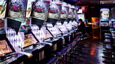 A man plays inside a modern arcade in Tokyo, illuminated by neon lights and gaming machines.