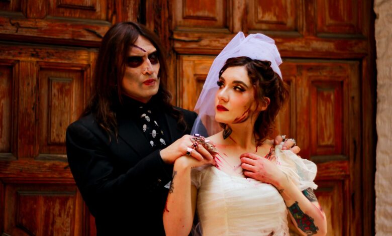 A couple in eerie Halloween wedding costumes posing with spooky makeup and props.