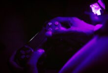 A close-up shot of hands gripping a gaming controller, illuminated by purple light, creating a vibrant atmosphere.