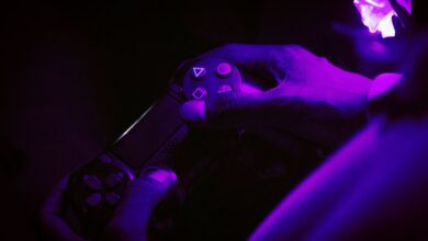A close-up shot of hands gripping a gaming controller, illuminated by purple light, creating a vibrant atmosphere.