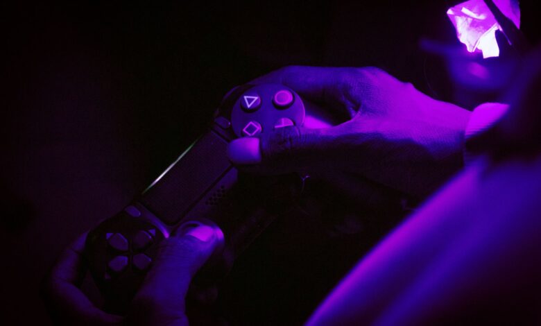 A close-up shot of hands gripping a gaming controller, illuminated by purple light, creating a vibrant atmosphere.