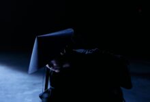 A mysterious figure in cosplay costume with a sakkat in a dark studio setting, conveying intrigue and concept.
