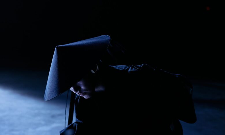 A mysterious figure in cosplay costume with a sakkat in a dark studio setting, conveying intrigue and concept.