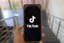 A close-up of a hand holding a smartphone displaying the TikTok app inside a modern building.