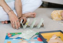 Hands building a card house on a carpet, capturing a playful and intimate moment indoors.