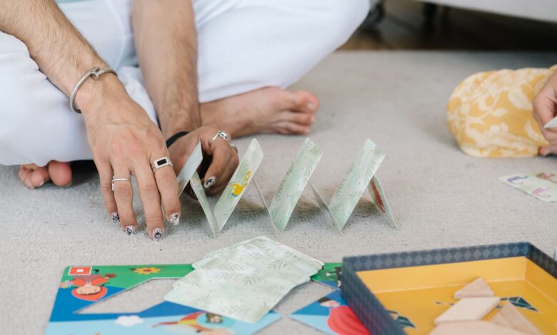 Hands building a card house on a carpet, capturing a playful and intimate moment indoors.