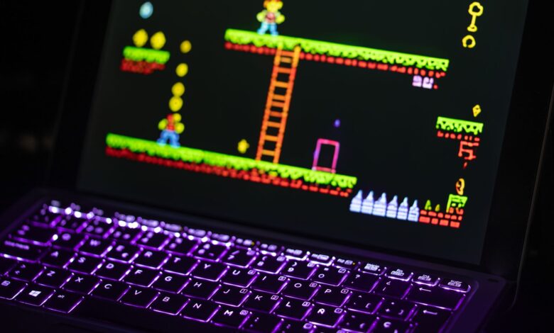 Close-up of a laptop displaying a retro video game with a neon-lit keyboard, capturing the nostalgic gaming experience.