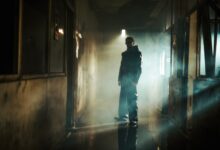 A man in dark attire stands in a smoky, shadowy corridor, creating a mysterious vibe.