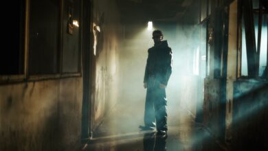 A man in dark attire stands in a smoky, shadowy corridor, creating a mysterious vibe.