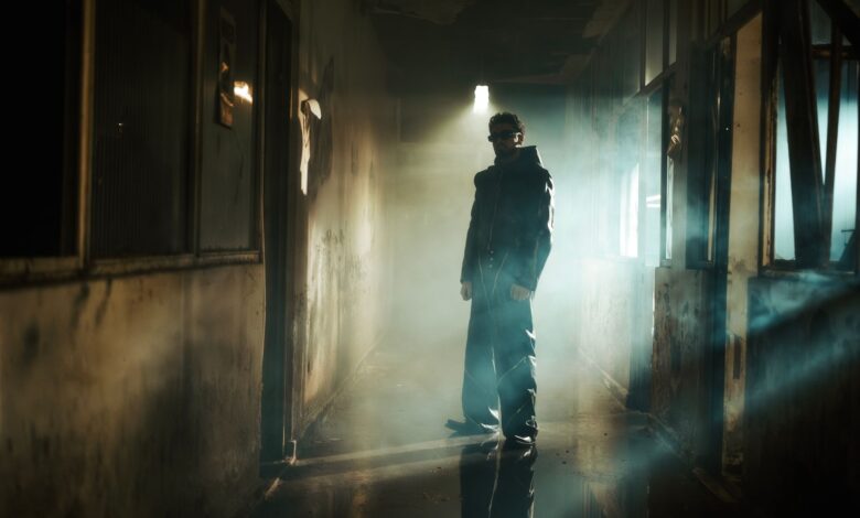 A man in dark attire stands in a smoky, shadowy corridor, creating a mysterious vibe.
