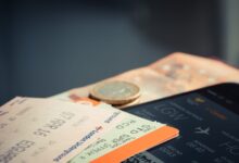 Airline ticket with euro coins and smartphone displaying flight details.