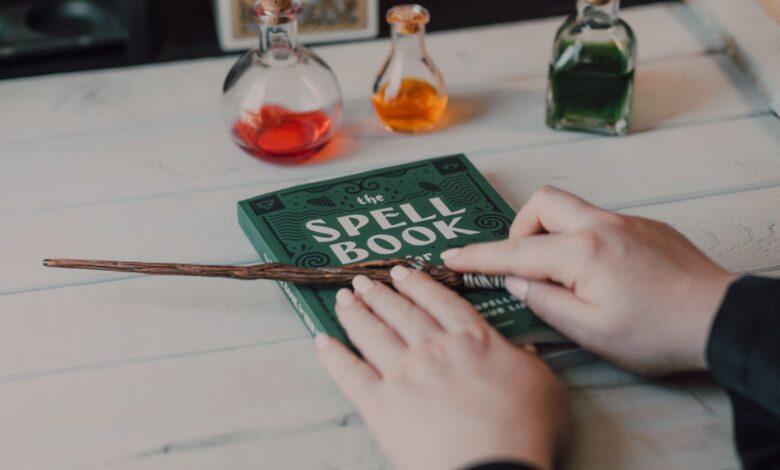 Close-up of hands with spell book, wand, and colorful potions on a table.