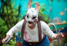 A person in a terrifying rabbit mask performs horror cosplay outdoors amid vibrant greenery.