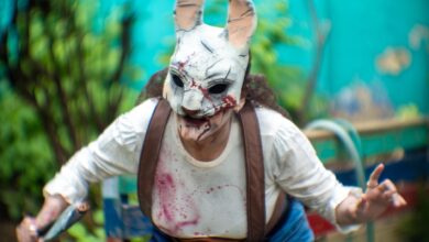 A person in a terrifying rabbit mask performs horror cosplay outdoors amid vibrant greenery.