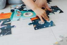Close-up of a child's hands solving a colorful space-themed jigsaw puzzle on the floor.