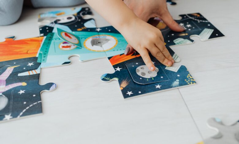 Close-up of a child's hands solving a colorful space-themed jigsaw puzzle on the floor.