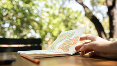 A hand flipping through a sketchbook with colorful drawings in a lush outdoor setting.