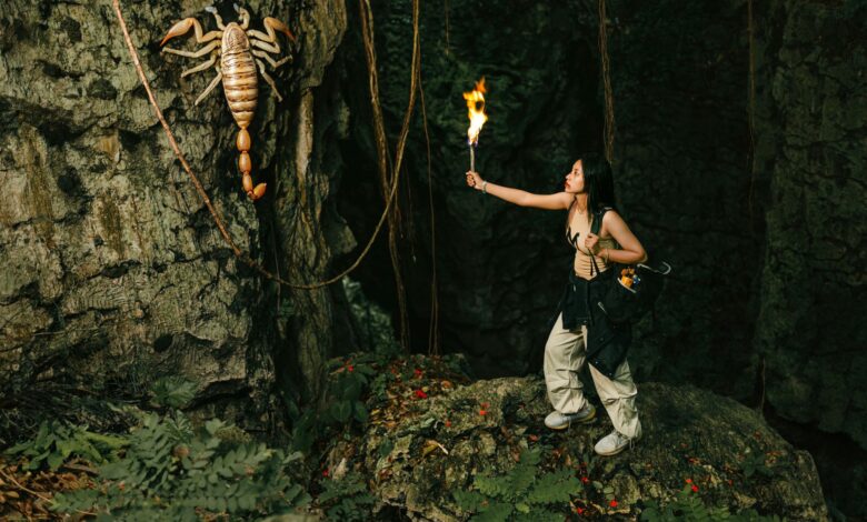 An adventurous woman explores a cave, wielding a torch against a giant scorpion.