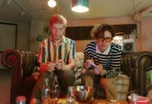 Two young men enjoying a video game night in a retro-inspired basement setting.