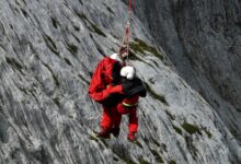 Two rescuers in action on a mountain, showcasing teamwork and safety in a daring lift.