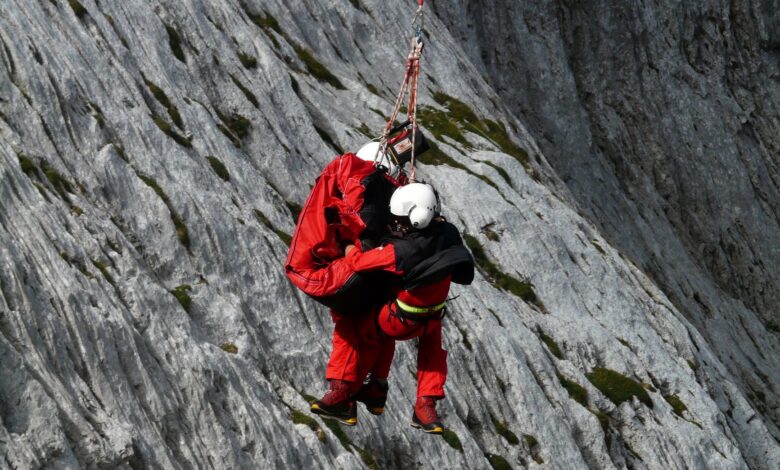 Two rescuers in action on a mountain, showcasing teamwork and safety in a daring lift.