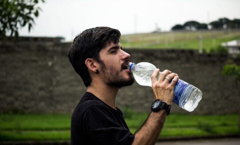 A young man drinks bottled water outside, staying hydrated and refreshed.
