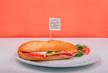Fresh sub sandwich filled with veggies on a white plate against an orange background.