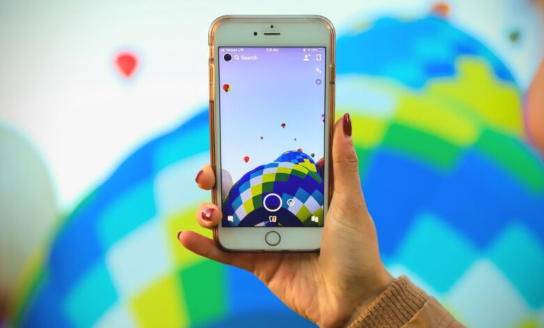 A person photographs a colorful hot air balloon festival using a smartphone, showcasing technology and travel.