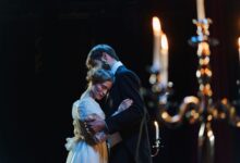 A romantic embrace on stage between actors in elegant costumes under warm lighting.