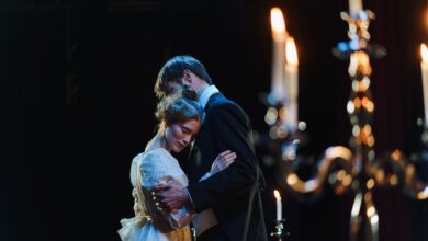 A romantic embrace on stage between actors in elegant costumes under warm lighting.