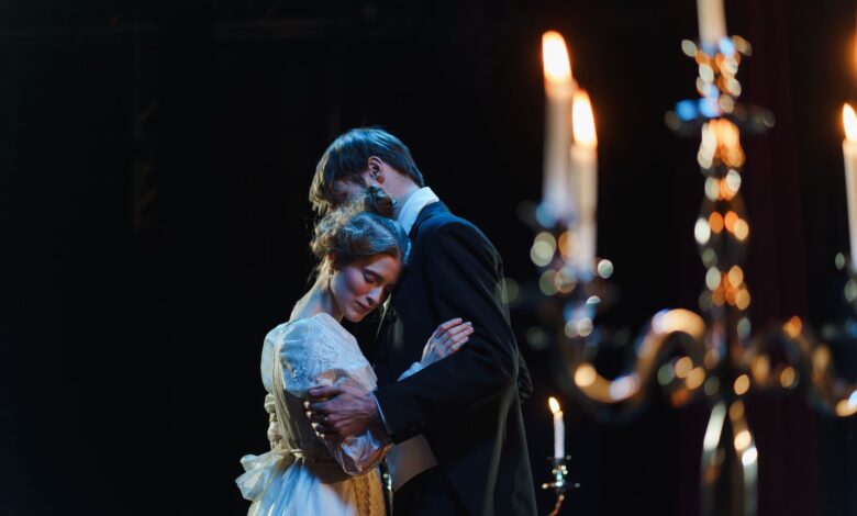 A romantic embrace on stage between actors in elegant costumes under warm lighting.