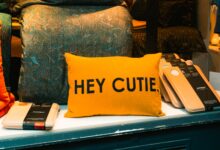 A vibrant yellow pillow with 'HEY CUTIE.' text displayed in a cozy shop setting in Freiburg, Germany.
