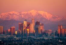 Stunning view of Los Angeles skyline with snow-capped mountains at sunset.