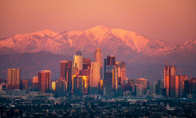Stunning view of Los Angeles skyline with snow-capped mountains at sunset.