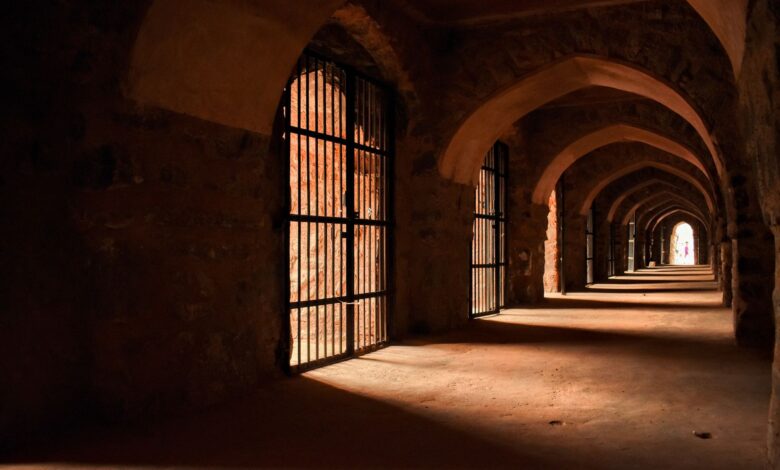 Dramatic lighting in an ancient stone corridor with gothic arches and barred gates.