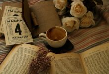 Aesthetic setup of coffee, books, and white roses on a cozy blanket.