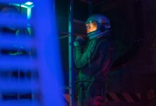 A female astronaut in a spacesuit stands in a neon-lit space shuttle, ready for interstellar exploration.