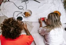 Two friends enjoying a video game session with snacks on the floor indoors.