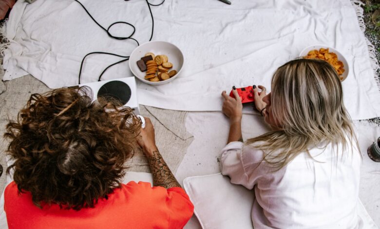 Two friends enjoying a video game session with snacks on the floor indoors.