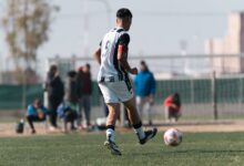 Young soccer player dribbles on field during a bright day match with spectators.