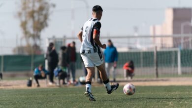 Young soccer player dribbles on field during a bright day match with spectators.