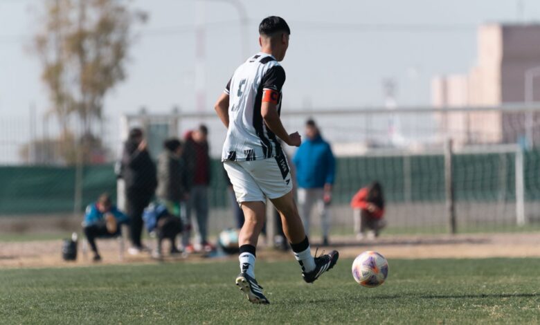 Young soccer player dribbles on field during a bright day match with spectators.