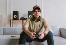 Casual scene of a young man playing video games on the couch with headphones and controller.
