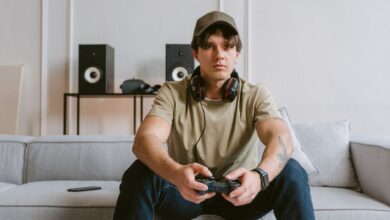 Casual scene of a young man playing video games on the couch with headphones and controller.