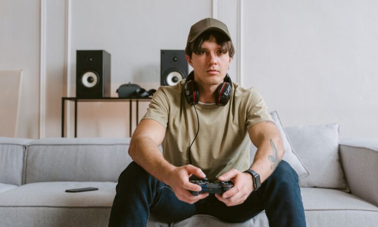 Casual scene of a young man playing video games on the couch with headphones and controller.