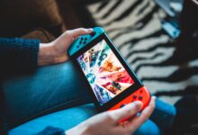 Person gaming on a handheld Nintendo Switch console with blurred background.