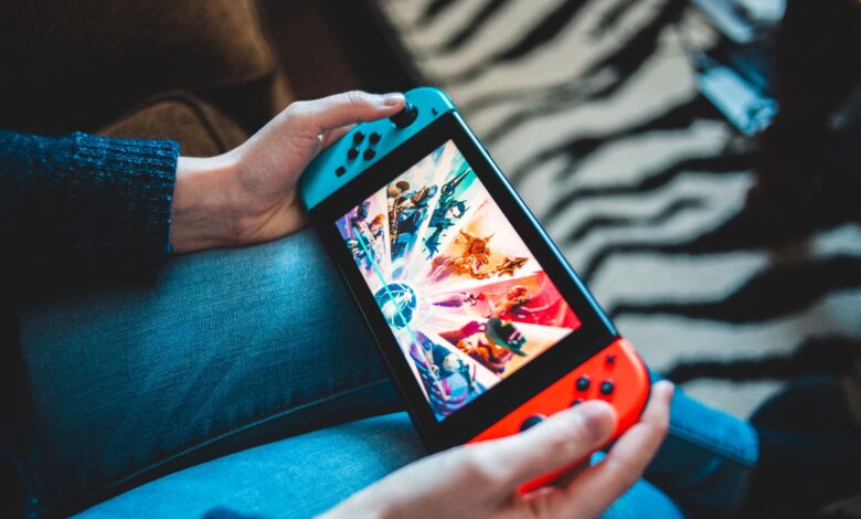 Person gaming on a handheld Nintendo Switch console with blurred background.