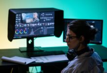 Focused video editor working at a dual-screen setup with colorful lighting ambiance.