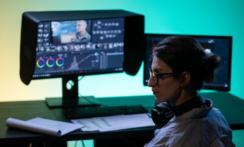 Focused video editor working at a dual-screen setup with colorful lighting ambiance.