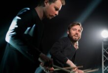 Dynamic drummers performing live on stage with focused lighting.